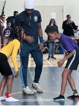 Wrestling coach referees two children wrestling in a gym.